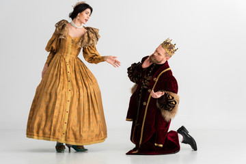queen talking and king with crown bending on knees on grey background