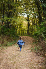 A little girl in a denim suit runs along a forest path. A girl walks in the autumn forest and plays with rubber snakes