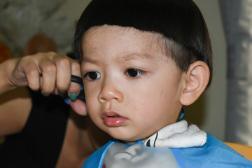 mother hairdresser using scissor haircut a cute baby boy in home