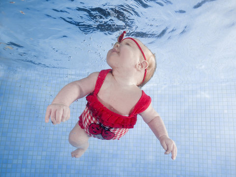 Newborn girl in a red swimsuit learns to dive in a swimming pool
