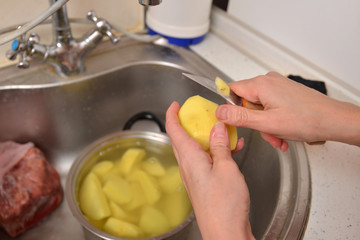 Woman housewife peels potatoes with a knife in the sink over the sink.