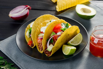 Appetizing hard-shell tacos with avocado, beef, tomato, cilantro and sour cream