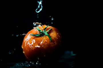 Czerwony pomidor polewany wodą, czarne tło
