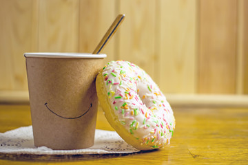 Paper cup of coffee and donut with icing on a wooden table. The concept of a quick breakfast, snack.