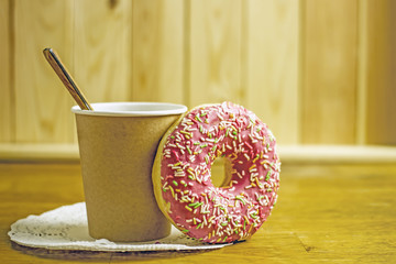 Paper cup of coffee and donut with icing on a wooden table. The concept of a quick breakfast, snack.