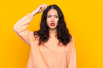 Spanish Chinese woman over isolated yellow background having doubts while scratching head