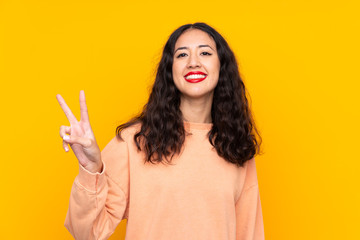 Spanish Chinese woman over isolated yellow background smiling and showing victory sign