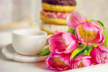 Festive breakfast. Flowers and donuts close-up. Delicious breakfast of pink icing donuts, coffee cup, pink tulips. Romantic background about love, valentine's day, birthday, mother's day