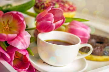 Fototapeta na wymiar Festive breakfast. Flowers and donuts close-up. Delicious breakfast of pink icing donuts, coffee cup, pink tulips. Romantic background about love, valentine's day, birthday, mother's day
