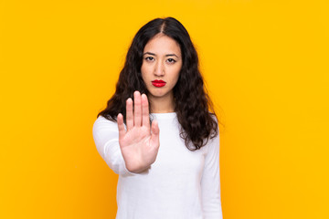 Mixed race woman over isolated yellow background making stop gesture with her hand