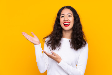 Mixed race woman over isolated yellow background extending hands to the side for inviting to come