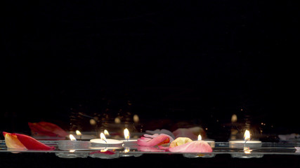 Candles floating on the water and falling rose petals