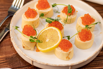 Dough rolls with cheese, red caviar. Garnished with sprigs of microgreen, a slice of lemon. On a wooden natural background.