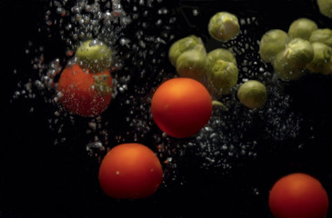 Brussels sprouts and tomatoes falling into the water with a splash