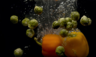 Fototapeta na wymiar Brussels sprouts and paprika falling into the water with a splash and bubbles