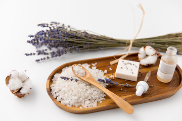 beauty and wellness concept - sea salt with spoon, soap, serum with dropper, lavender and cotton flowers on wooden tray