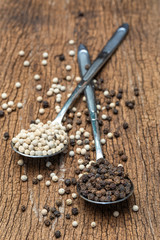 Close up of white peppers and black peppers on spoon on wooden background.