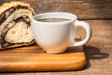 A white cup of hot coffee with bread on wooden background.