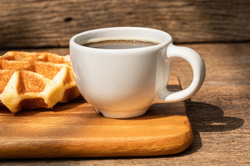 A white cup of hot coffee with waffle on wooden background.
