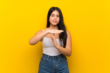 Young teenager Asian girl over isolated yellow background making time out gesture