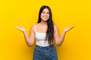 Young teenager Asian girl over isolated yellow background with shocked facial expression