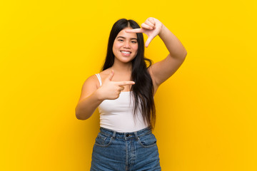Young teenager Asian girl over isolated yellow background focusing face. Framing symbol