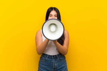 Young teenager Asian girl over isolated yellow background shouting through a megaphone