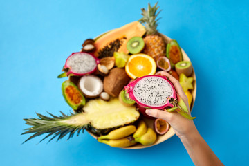 exotic food, summer and healthy eating concept - close up of hand holding half of dragon fruit over blue background