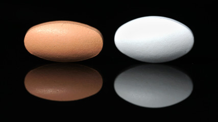 Two tablets with a reflection on a black background. The concept of medication.
