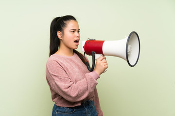 Young teenager Asian girl over isolated green background shouting through a megaphone