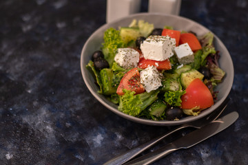 Greek vegetable salad. It consists of tomatoes, olives, feta cheese, herbs, cucumbers and red onions. On a wooden background.