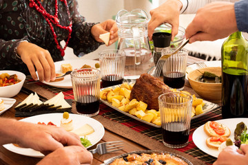 group of four people eating and drinking together at home - celerbating something with chicken and wine - hands taking food from the middle of the table