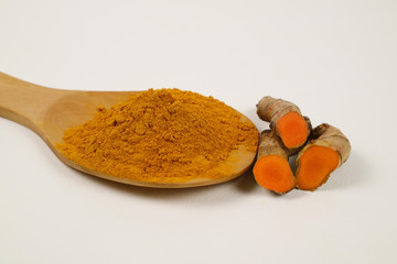 Turmeric powder in a wooden spoon and turmeric root extracted on a white background, used as a...