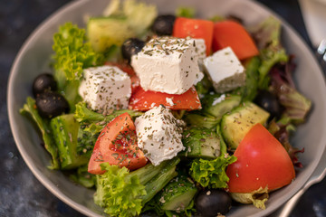 Greek vegetable salad. It consists of tomatoes, olives, feta cheese, herbs, cucumbers and red onions. On a wooden background.