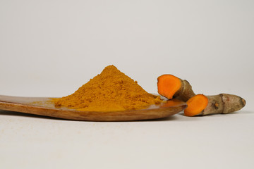 Turmeric powder and turmeric root in a wooden spoon isolated on a white background. Used as a tonic...