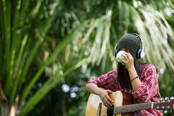 asian girl wearing a yarn hat, listening to music with headphones and drinking coffee in a white...