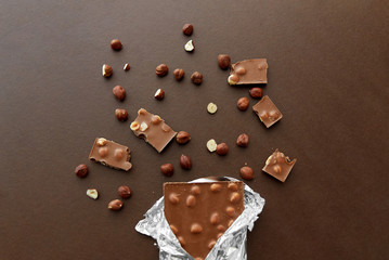 sweets, confectionery and food concept - milk chocolate bar with hazelnuts in foil wrapper on brown background