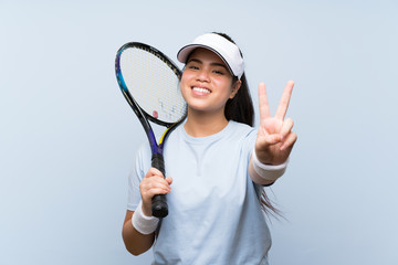 Young teenager Asian girl playing tennis smiling and showing victory sign