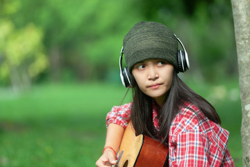 Fototapeta na wymiar asian girls wear knit hats and listen to music through earphones, ready to play guitar in the morning garden of the holidays