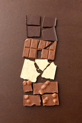 sweets, confectionery and food concept - milk, dark and white chocolate bars on brown background