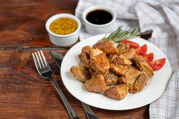 Fried and stewed chicken breast in soy-honey sauce. In the background mustard seeds. On a plate are slices of tomato and razmarin. On a wooden background.