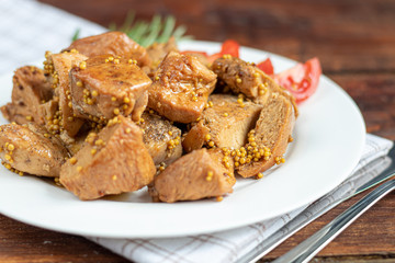 Fried and stewed chicken breast in soy-honey sauce. In the background mustard seeds. On a plate are slices of tomato and razmarin. On a wooden background.