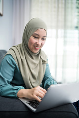 Female muslim using laptop at home environment.