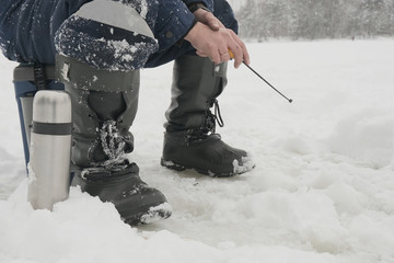 a fisherman in boots sits on the ice