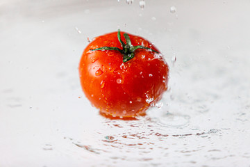 Świeży pomidor widziany z boku, polewany wodą © andsko