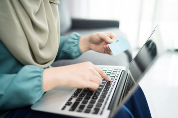 Female muslim woman using laptop while holding credit card.