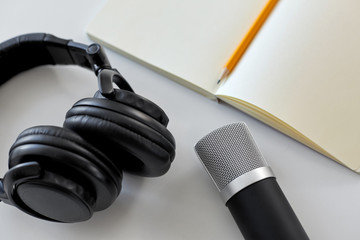 technology, sound recording and podcast concept - headphones , microphone and notebook with pencil...