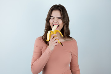 young beautiful woman biting fresh banana looking hungry being on diet isolated white background