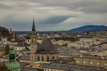 Obraz premium Salzburg old European city top view landmark heritage touristic site for visiting and sightseeing medieval houses roofs and cathedral building tower in moody weather time gray cloudy sky background