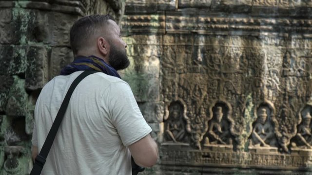 Man tourist taking photos of ancient Angkor Wat temple ruins in Cambodia